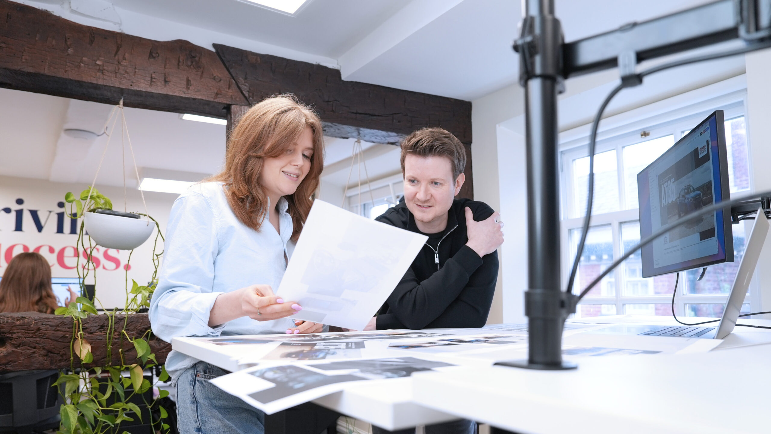 Woman and man at a standing desk looking over a selection of designs printed out on paper.