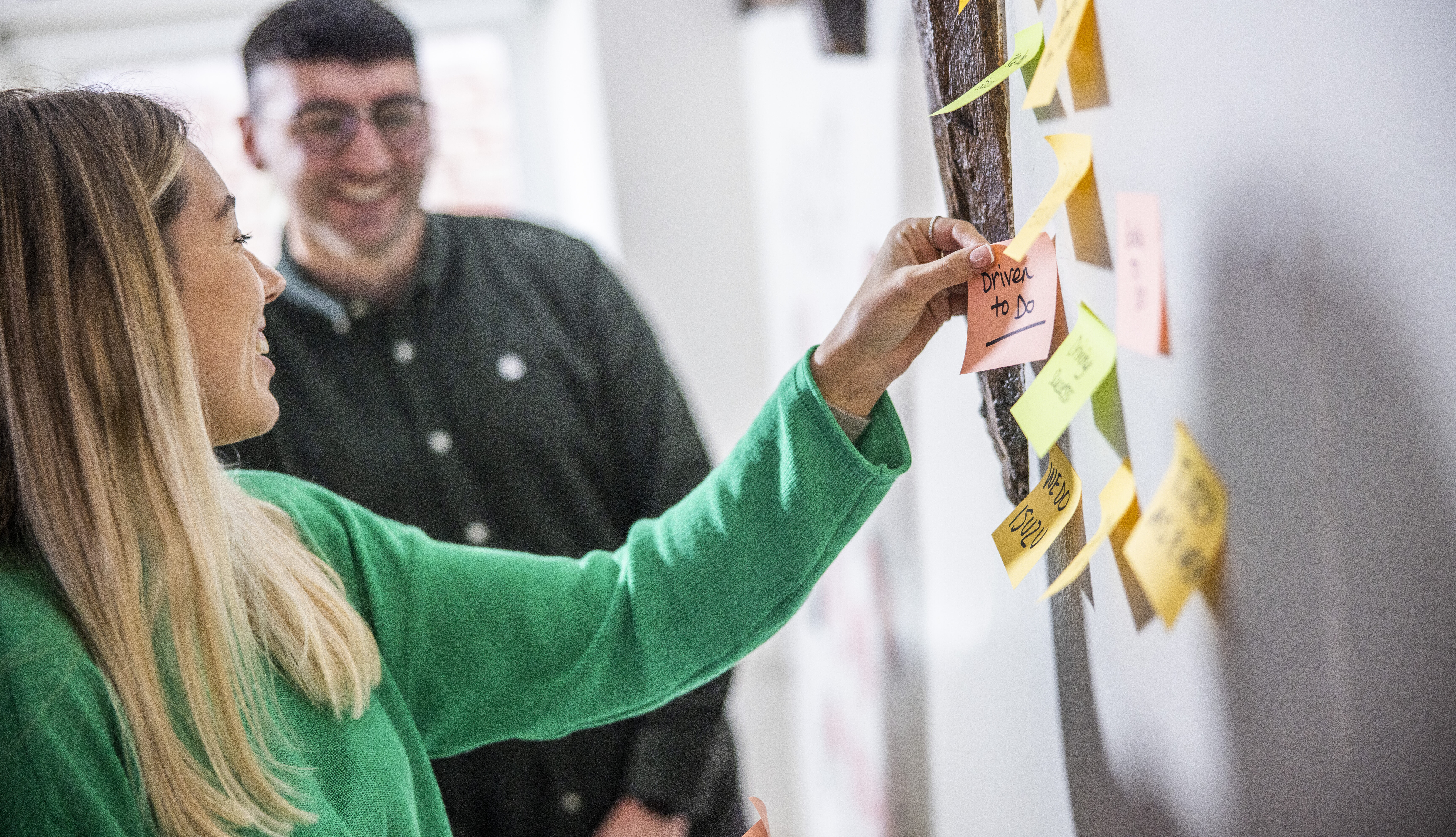 a woman in a green sweater putting post it notes on a wall.