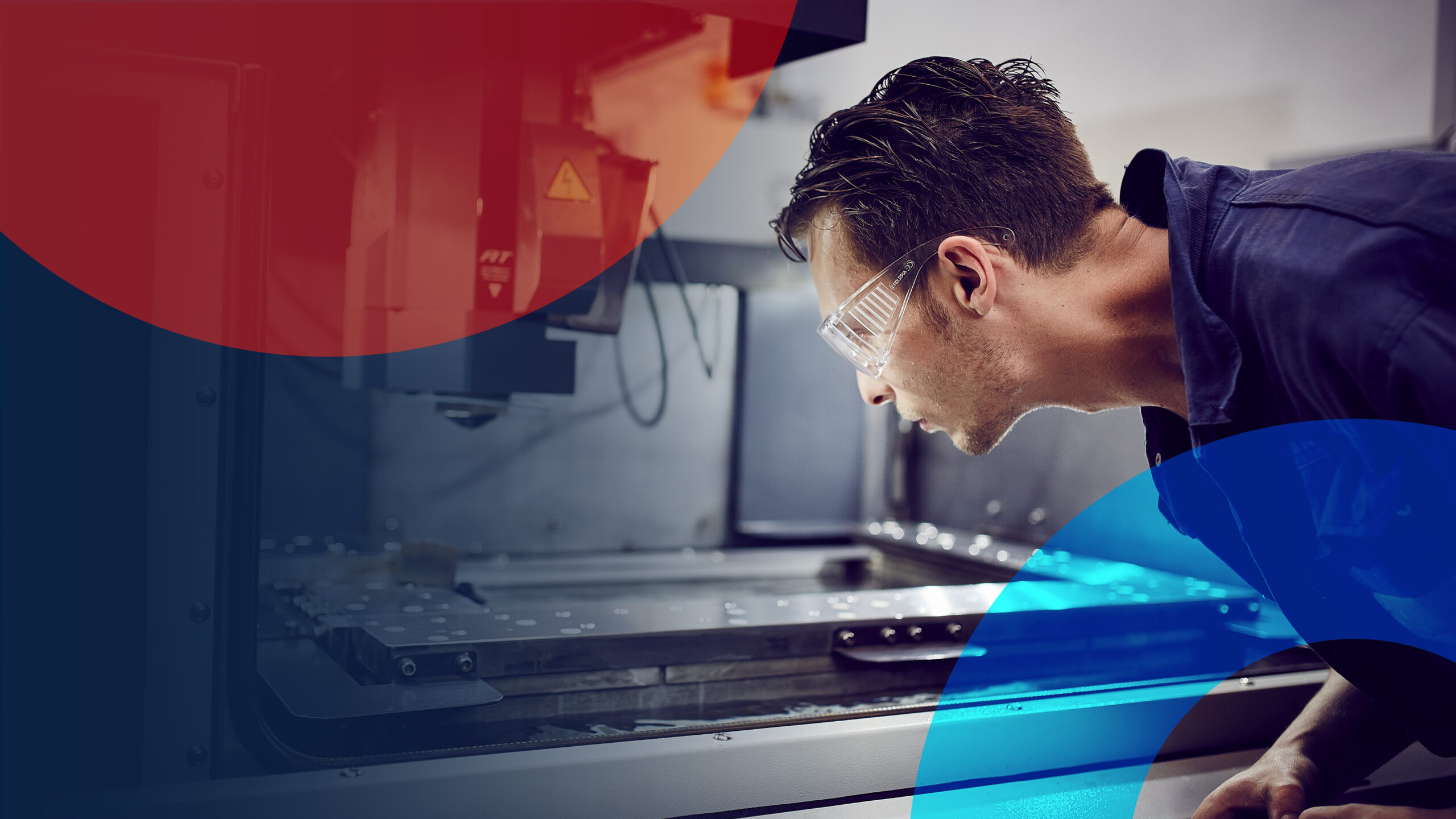 A technician wearing safety glasses leaning in to examine industrial manufacturing machinery, framed by red and blue geometric brand overlays.